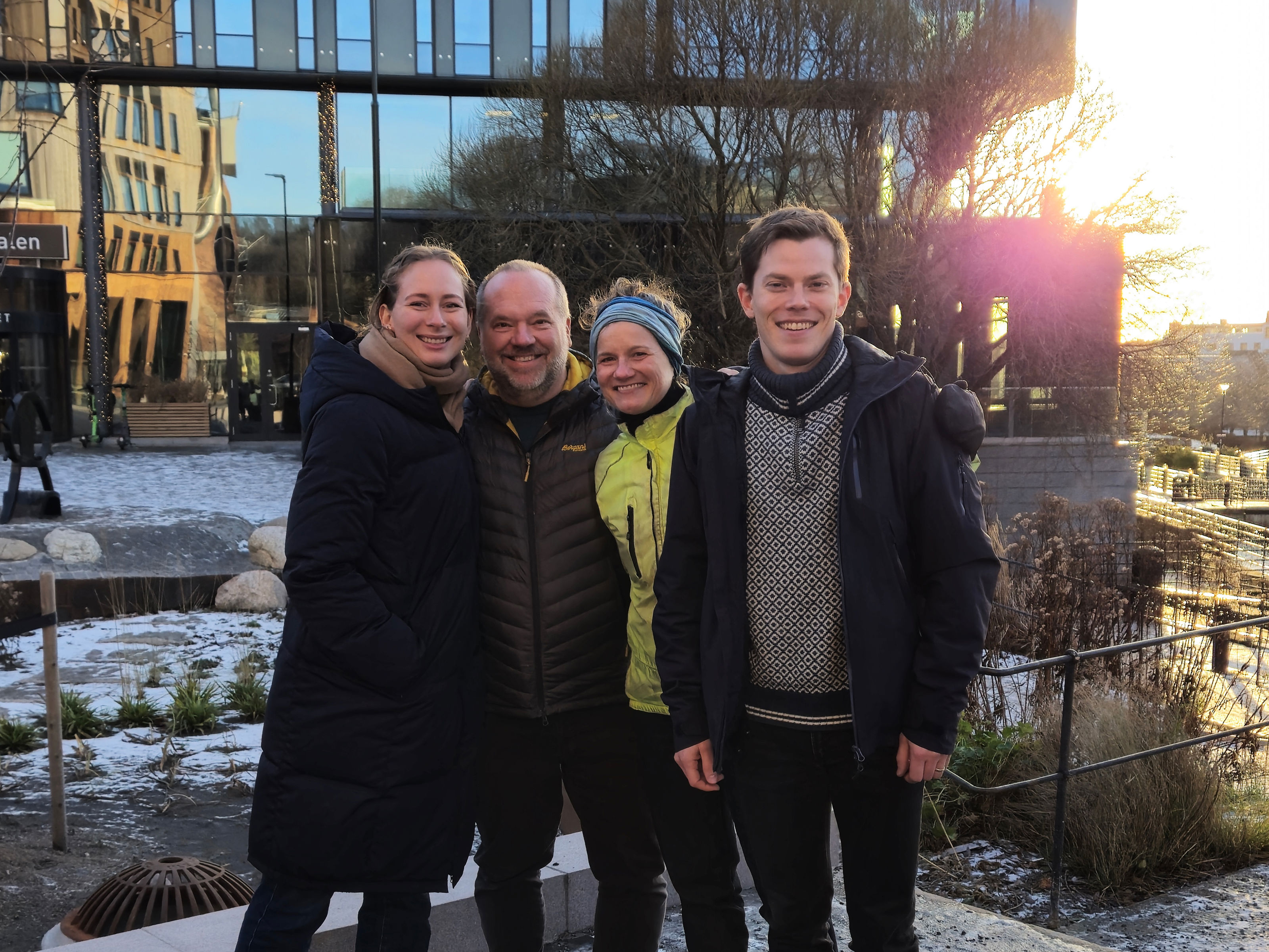 Fire mennesker står smilende og poserer foran kamera.